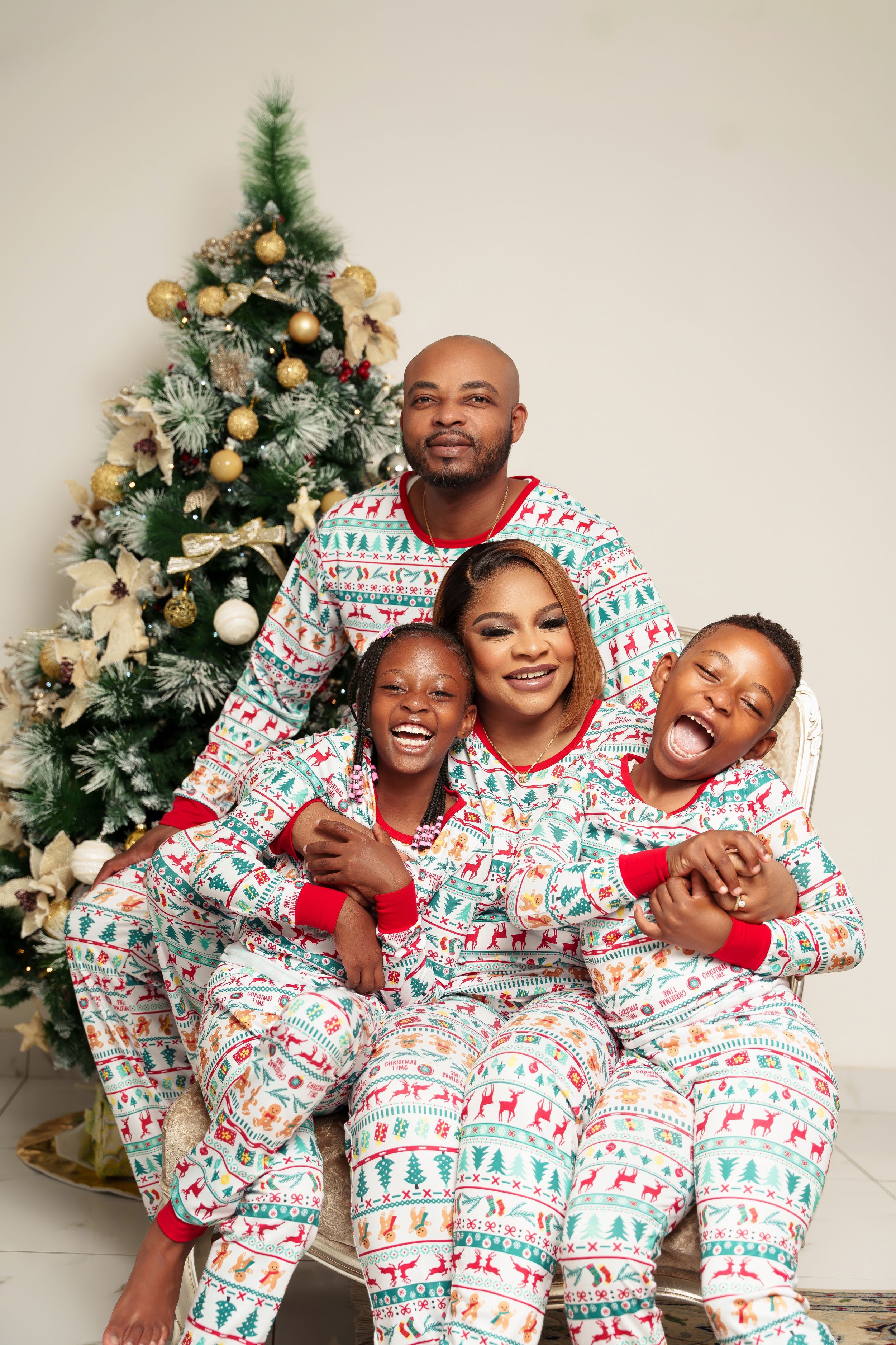 Family wearing matching Christmas pajamas poses playfully by decorated tree.