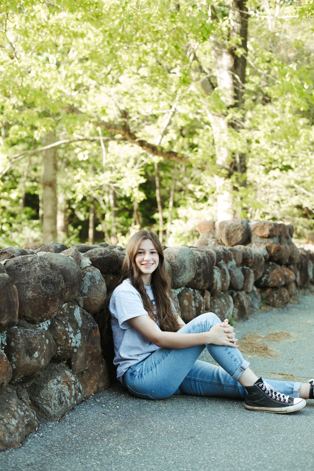 Casual portrait against stone wall with green foliage in background.