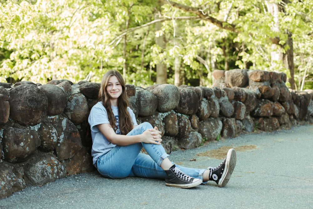 Student relaxes against rustic stone wall surrounded by spring greenery.