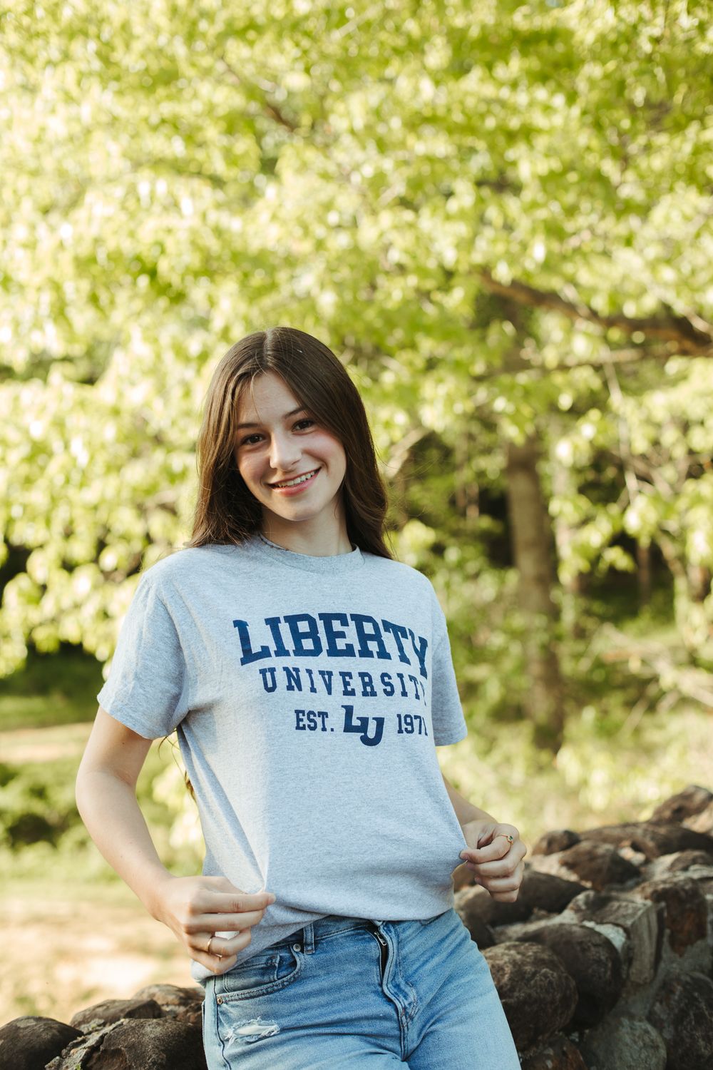 Student wearing Liberty University t-shirt poses on stone wall outdoors.