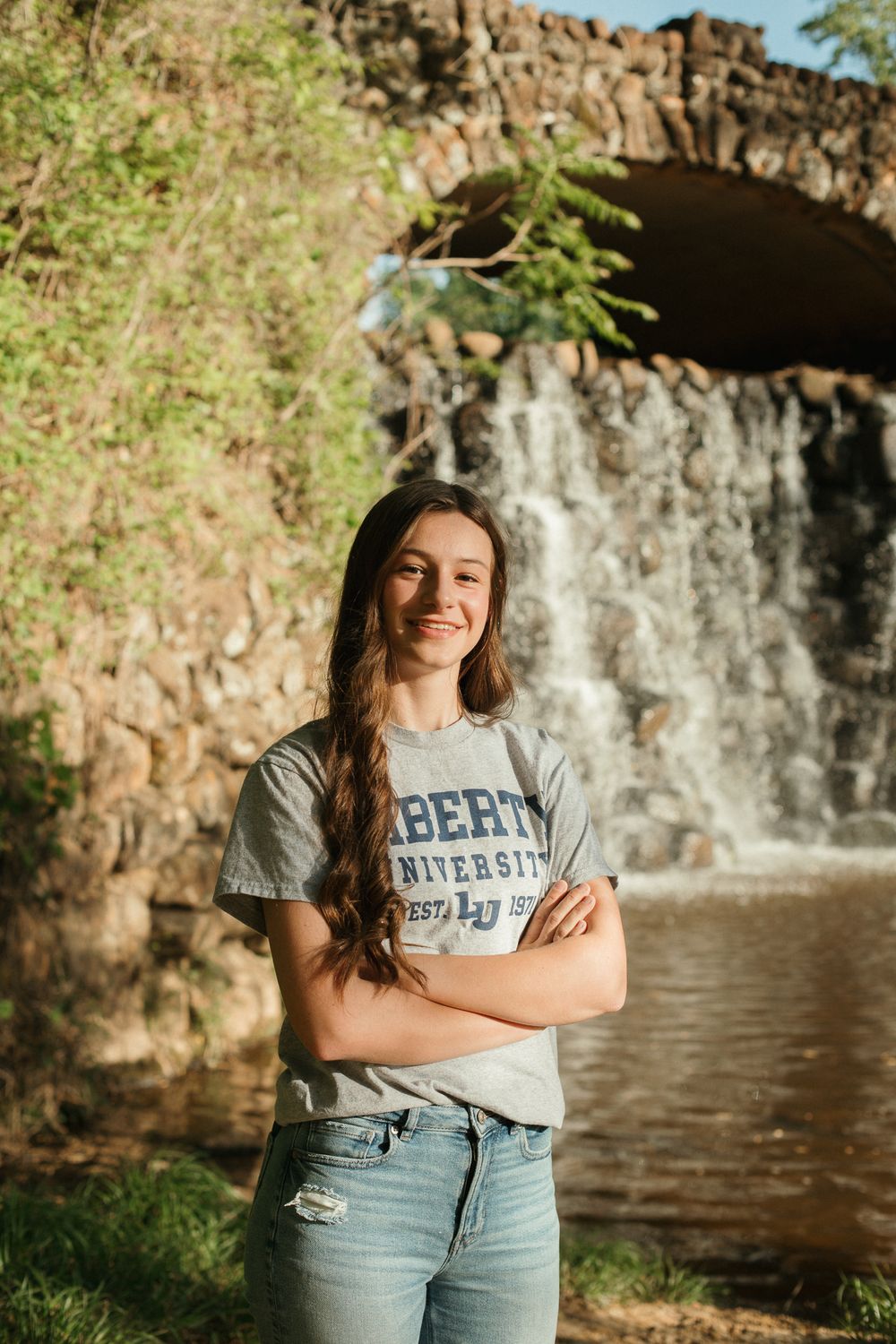 Student in Liberty University shirt poses near waterfall and stone wall.