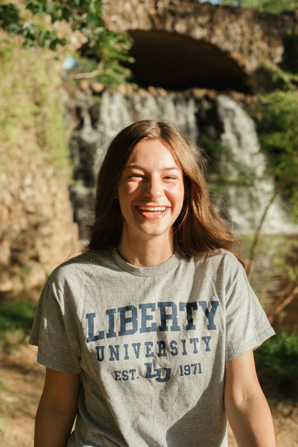 A Liberty University branded gray t-shirt being modeled outdoors with a rocky background.