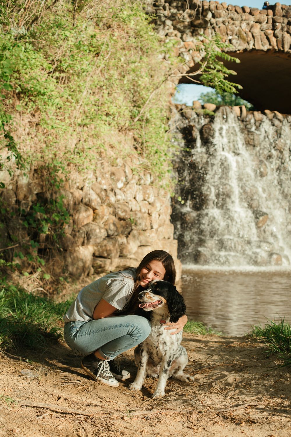 A playful moment between a person and their dog near a scenic waterfall.
