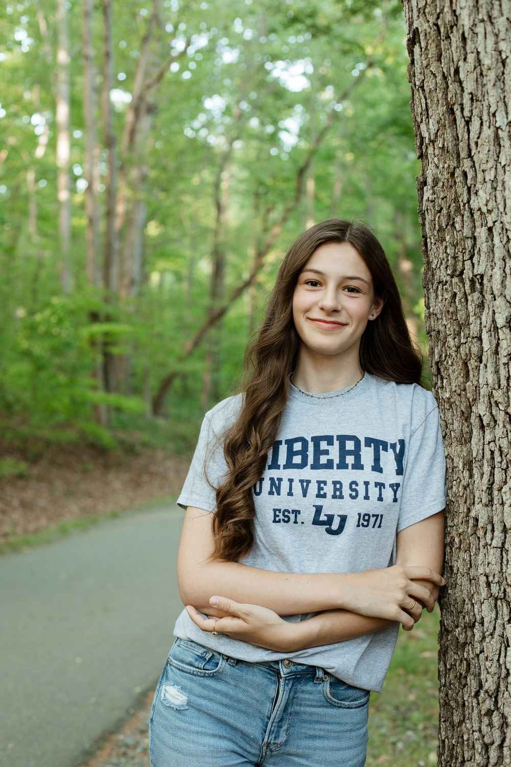 Someone wearing a Liberty University t-shirt poses against trees on a paved path.