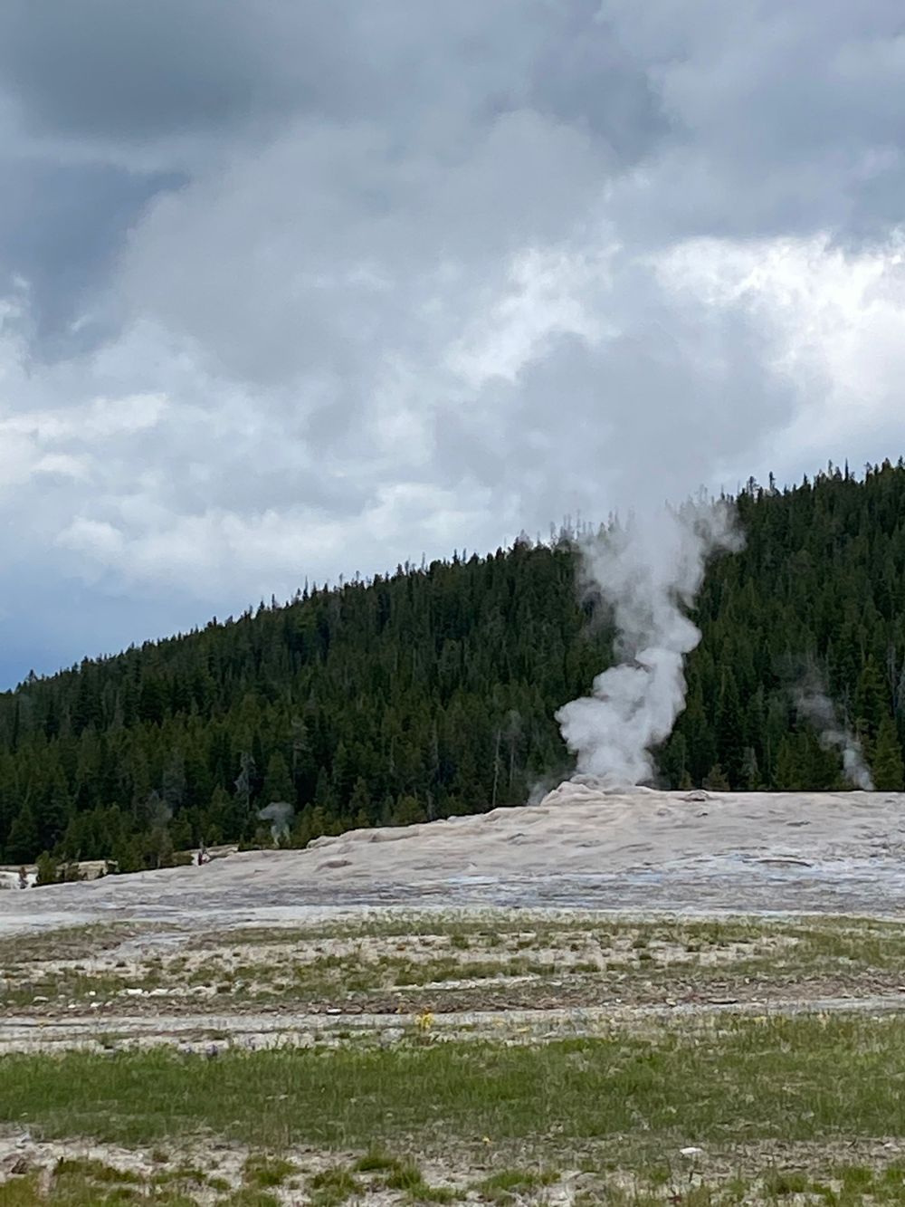 Steam rises from Old Faithful geyser under dramatic cloudy skies in Yellowstone National Park.