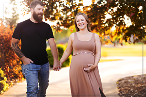 An expecting couple walks together on an autumn path during sunset.