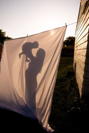 A silhouette of parent and child cast on a white sheet hanging on a clothesline at sunset.