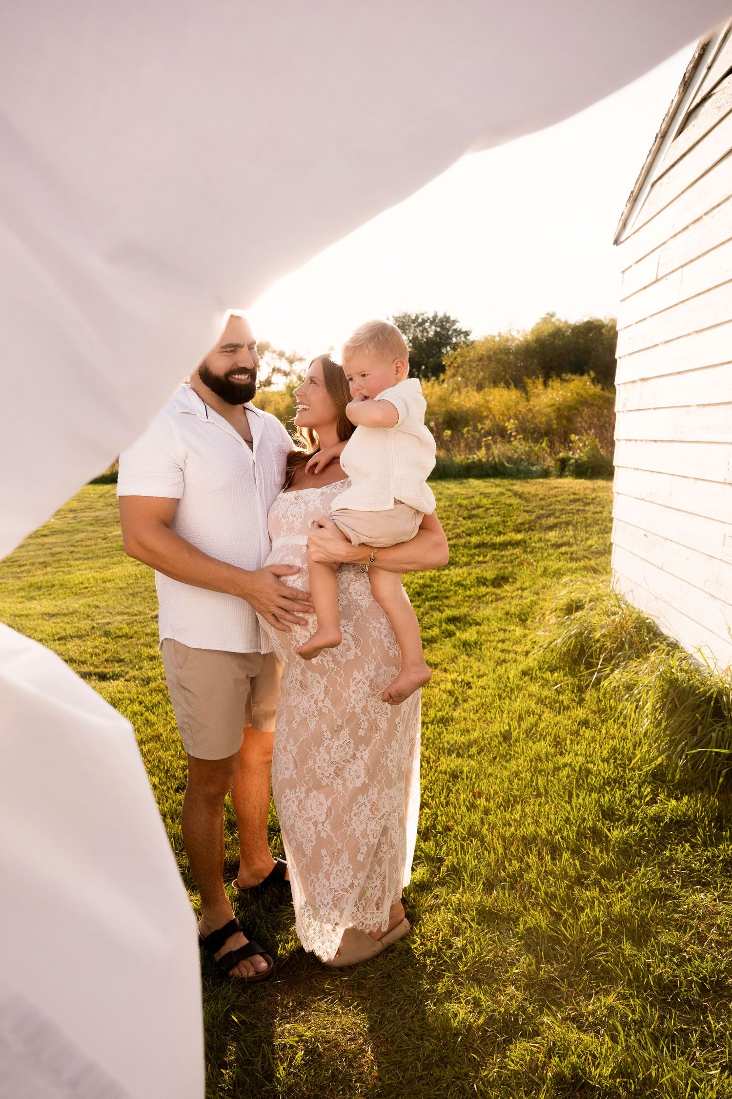 Family enjoying a warm sunset moment together on grassy lawn beside white building in summer.