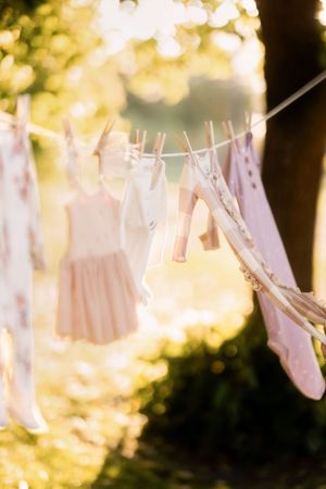 White laundry hangs on clotheslines outdoors with golden sunlight filtering through trees in the background.