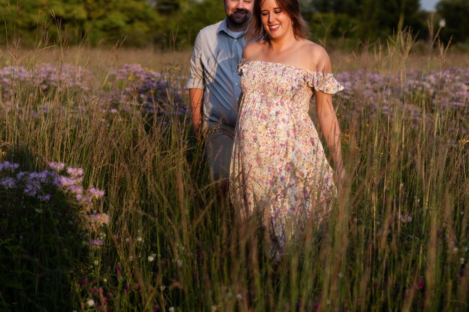 A couple shares a romantic moment together in a sunlit field of purple wildflowers at golden hour.