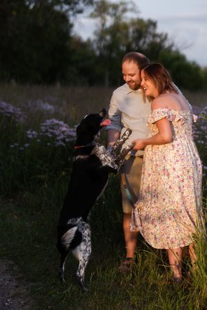 A couple in a floral field enjoying a moment with their black and white dog during golden hour.