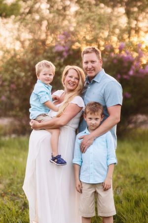 Family sharing candid laughs and embraces while posing together in a lush garden with purple flowers at sunset.