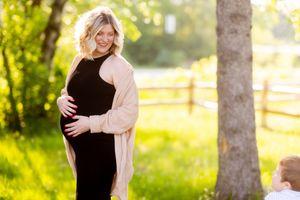 A couple embraces during an outdoor engagement photo session with golden sunlight filtering through trees.