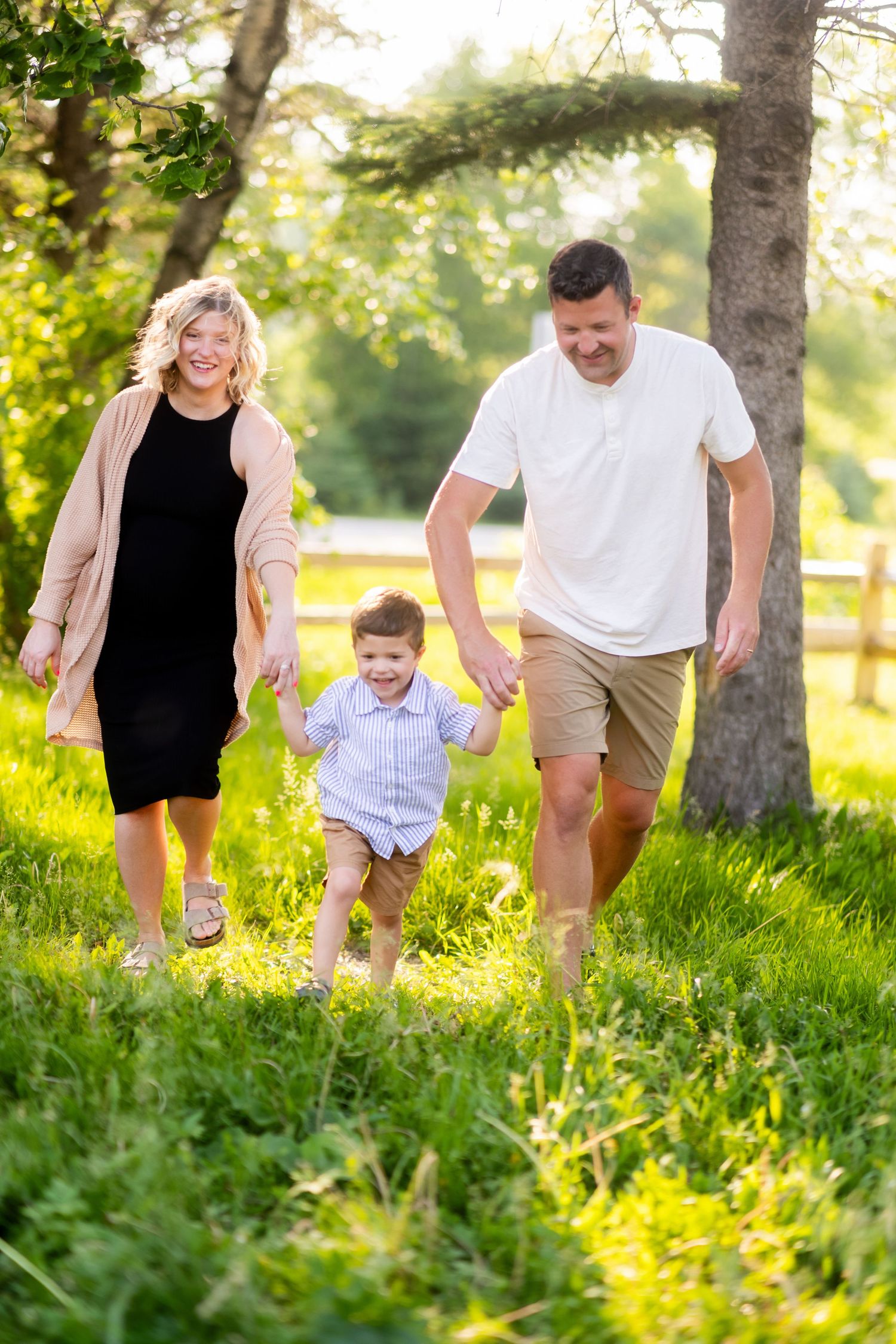 Family enjoying playful moment together in sunny park with tall trees and lush grass during golden hour.