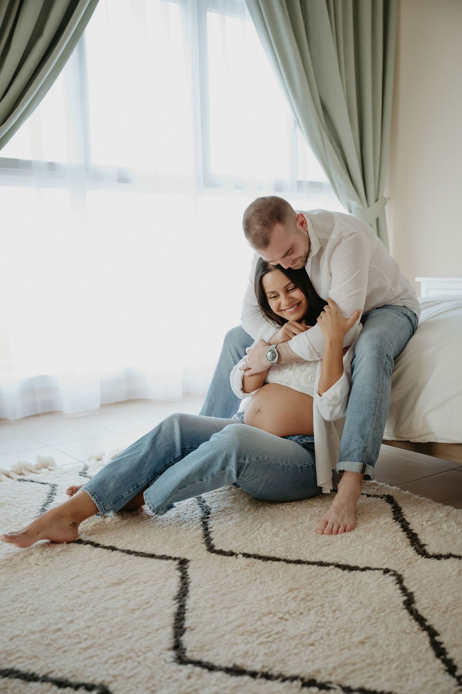 A tender maternity moment captured with dramatic lighting showing a couple embracing on the floor.