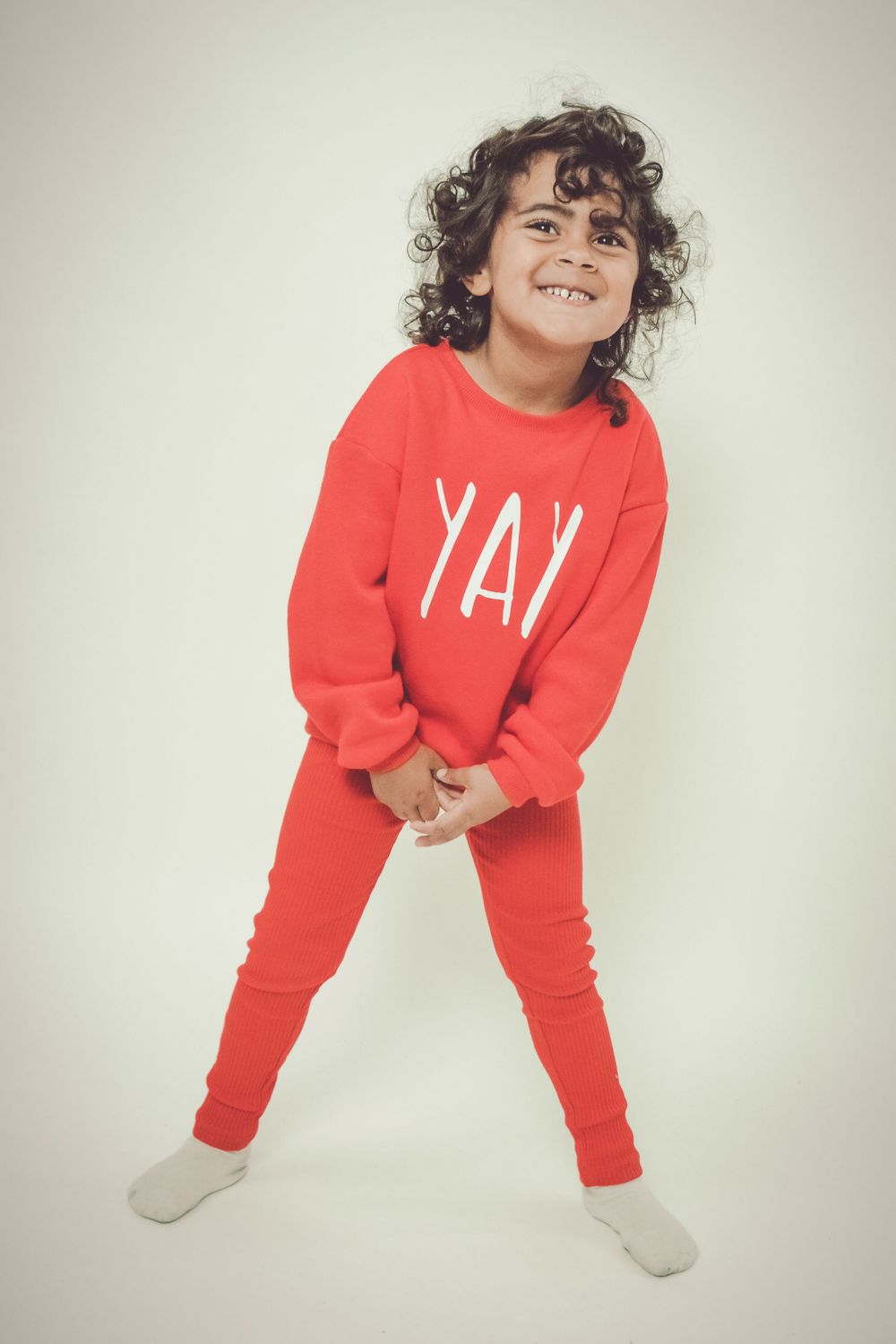 Child in bright red sweatsuit and socks poses playfully against white background in multiple candid shots.