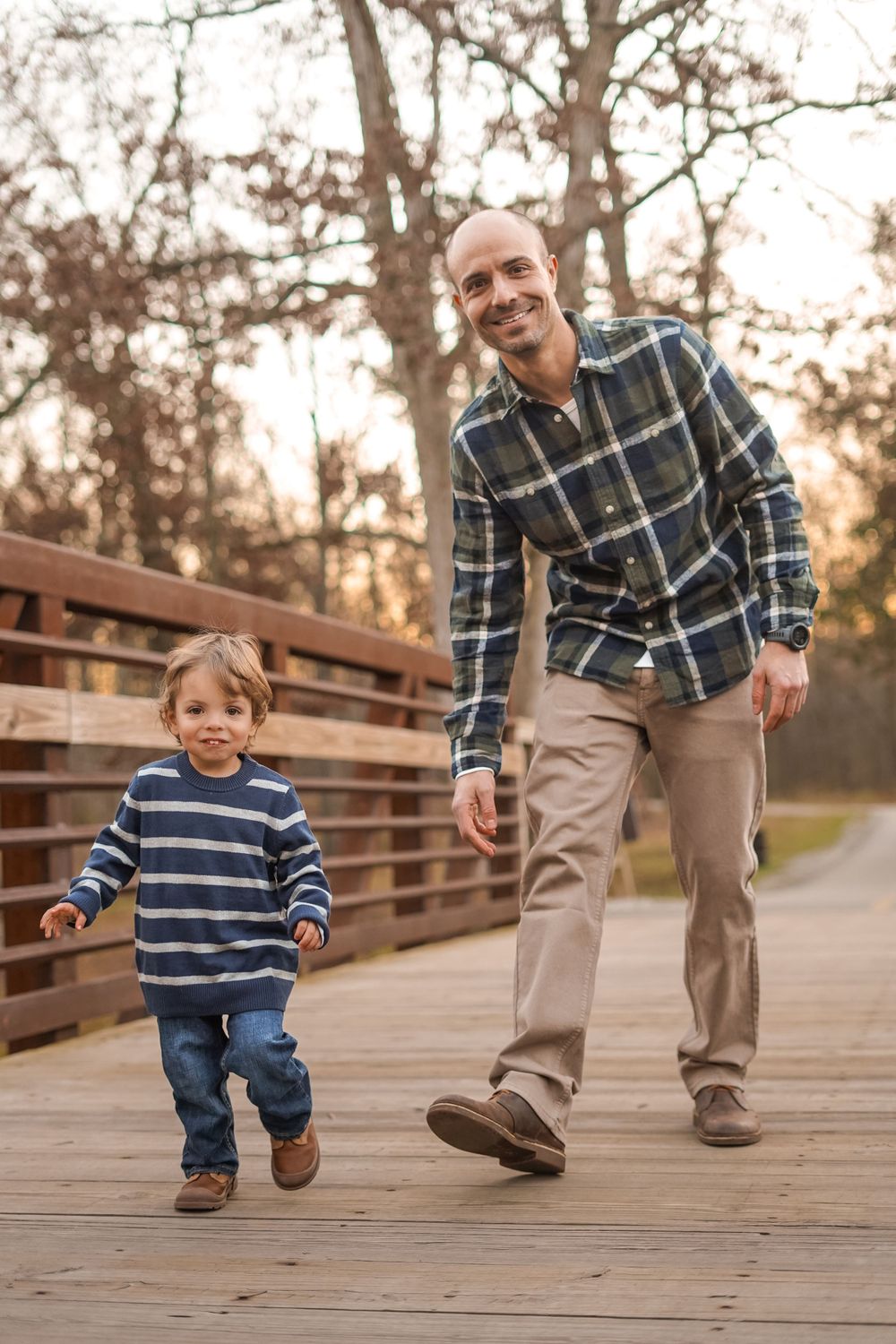 Parent and child walking together on a wooden bridge in casual attire.