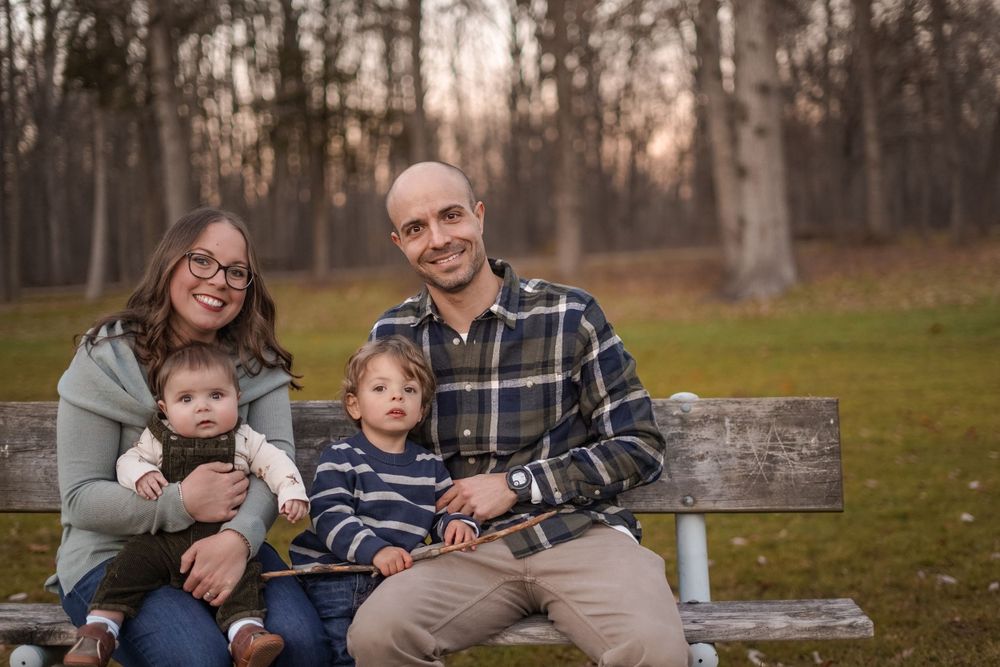 Family sitting together on wooden bench during golden hour outdoor photoshoot.