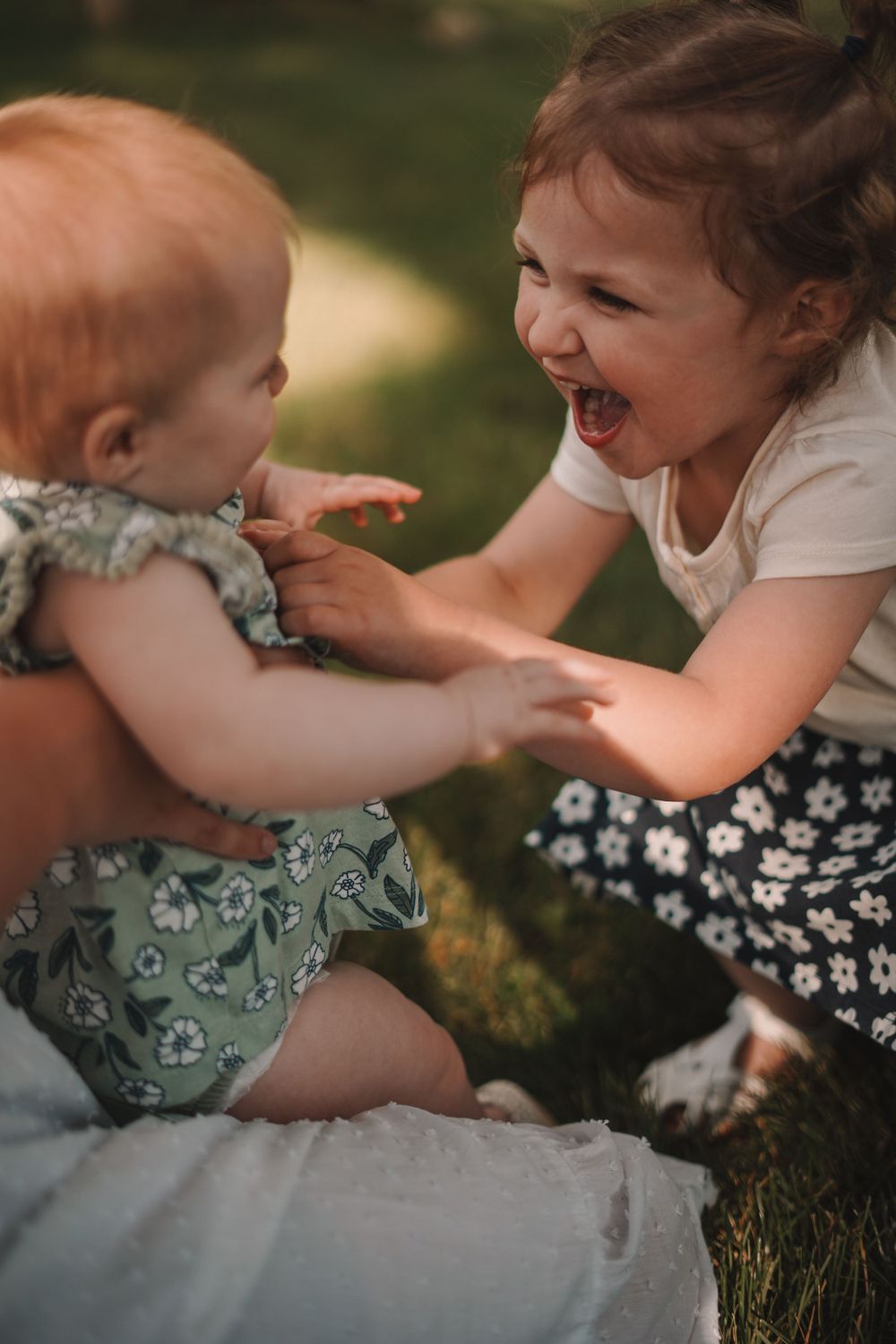 Children playing together on grass in floral dresses during summer.