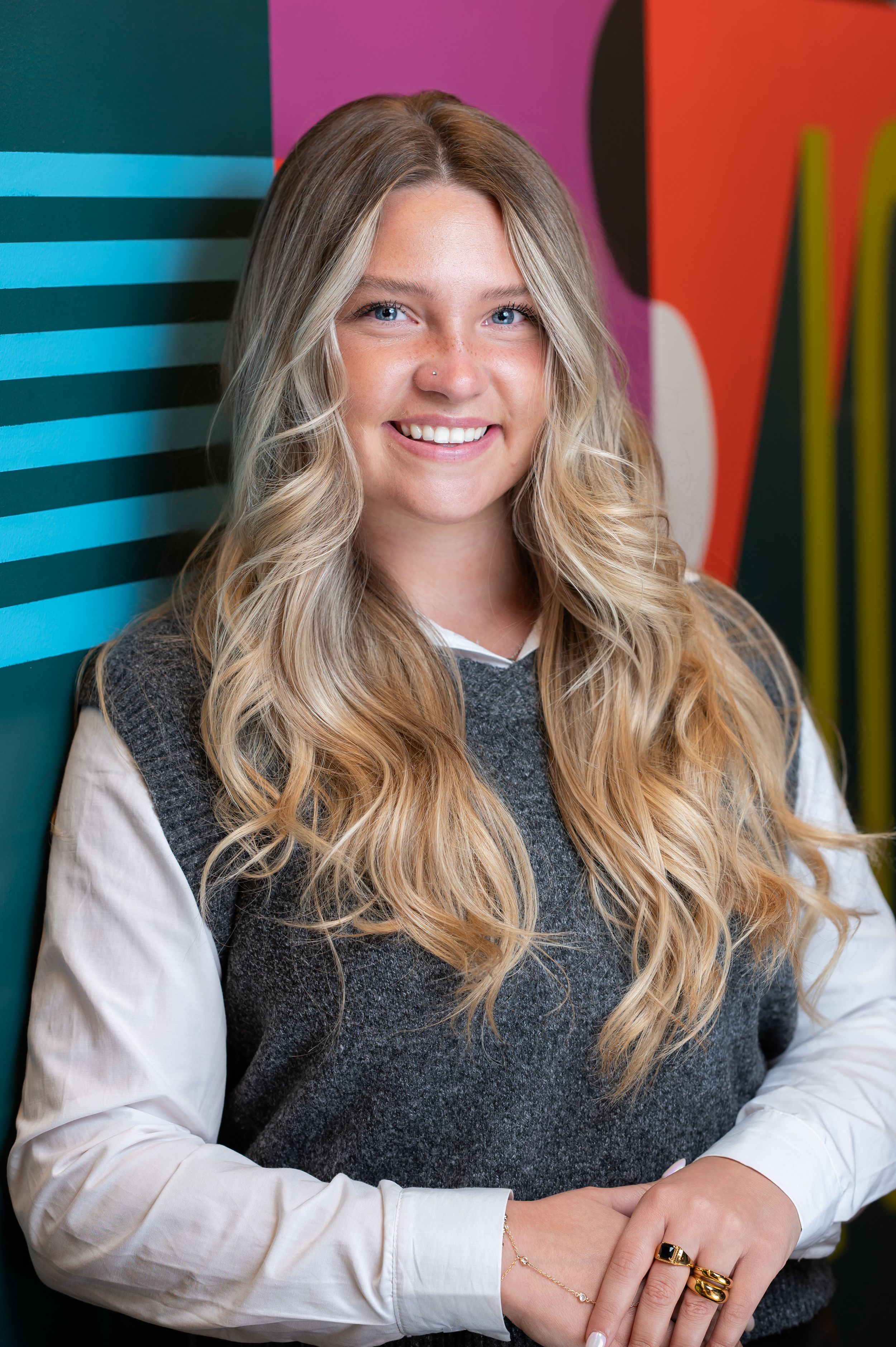 Professional portrait of someone wearing a gray vest over white long sleeve shirt against colorful geometric background.