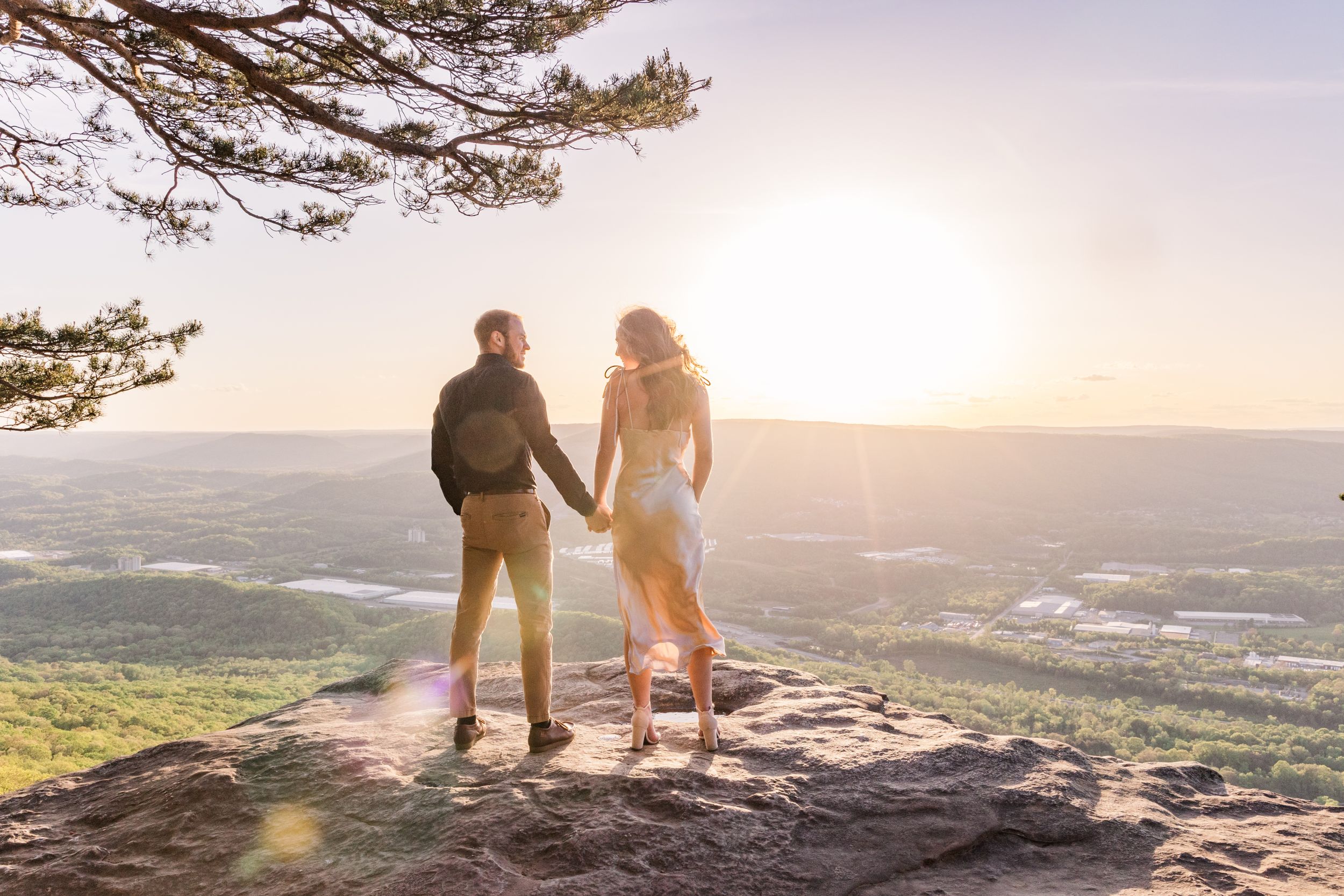 Couple standing together on mountain edge at golden sunset.