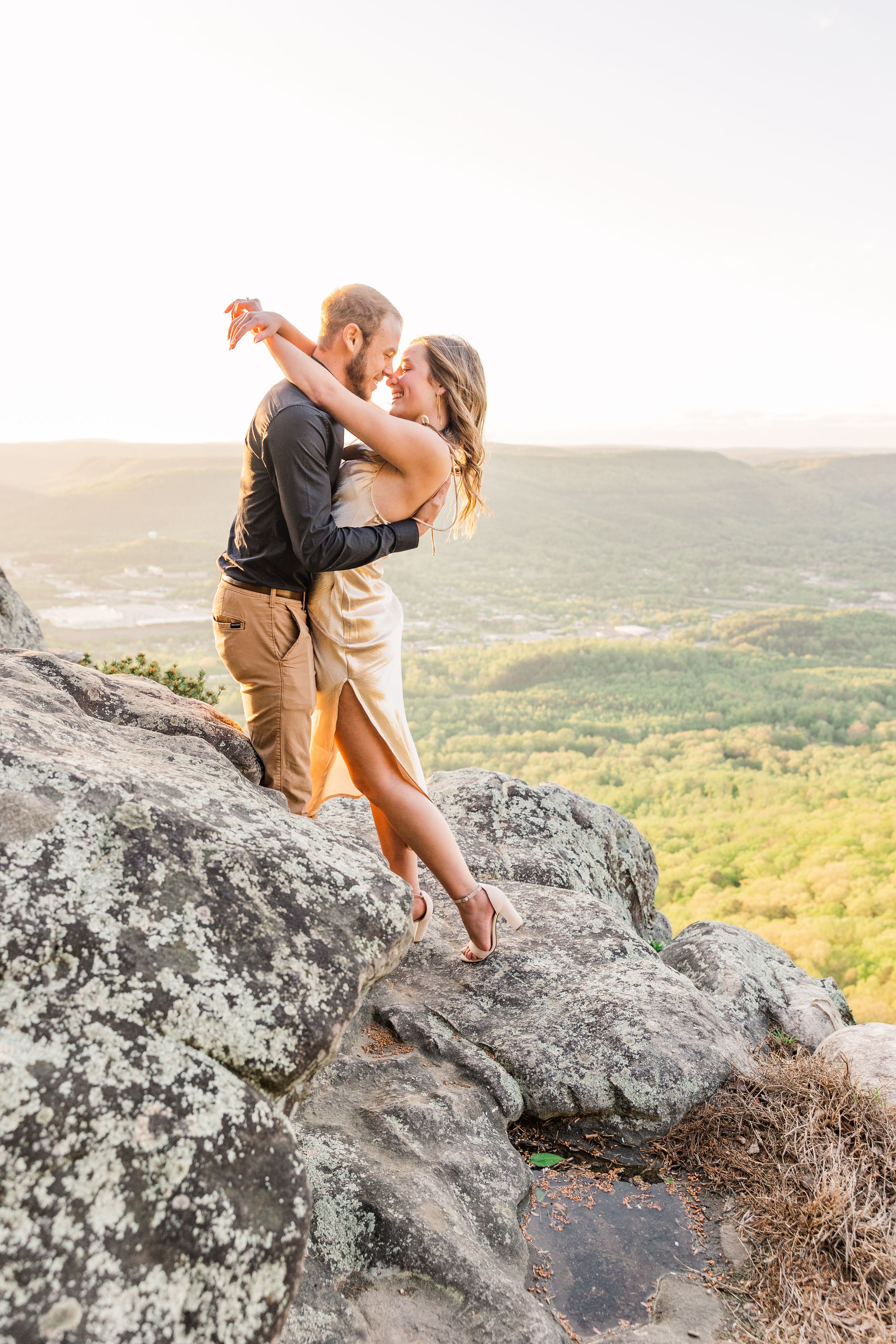 Romantic embrace on rocky cliff with sweeping valley views.