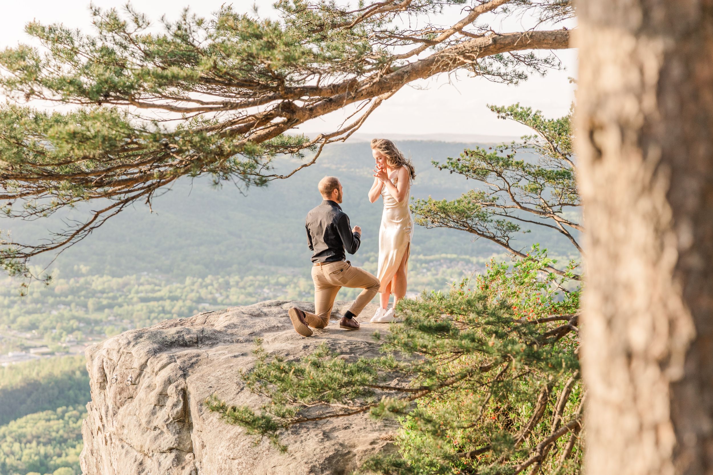 Romantic proposal moment on mountain overlook during sunset.