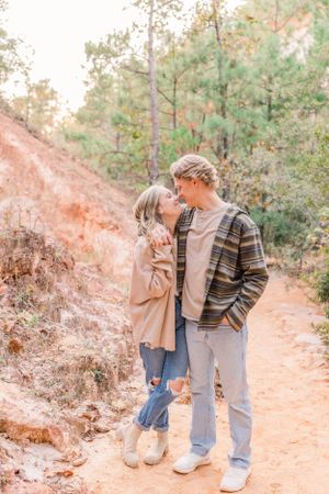 Couple in casual fall attire sharing a tender moment on a red clay hiking trail.