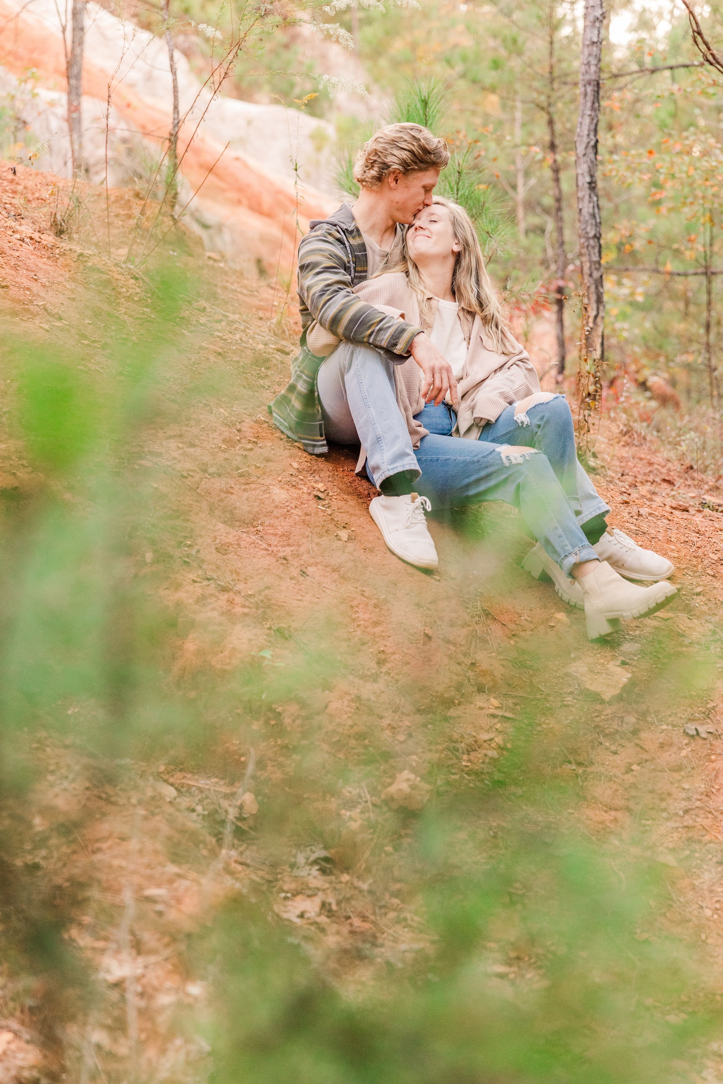 Couple sitting together on red clay slope surrounded by autumn foliage.