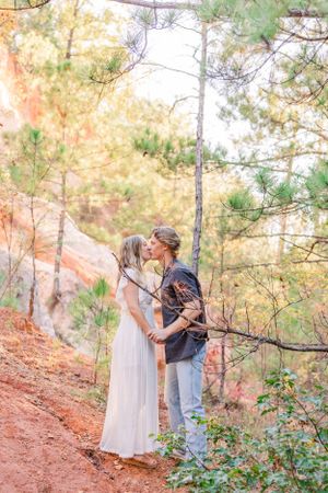 Romantic couple sharing an intimate moment on a red clay trail surrounded by pine trees during golden hour.