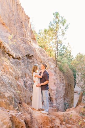 Couple embracing on rocky terrain with towering cliff face in background.