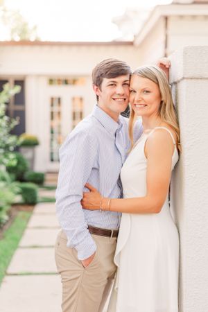 A couple poses against a white wall during their engagement photo session.