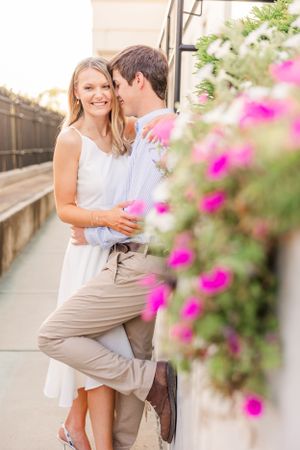 A couple shares an intimate moment near pink flowers during their engagement shoot.