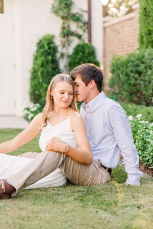 Couple sharing intimate moment while sitting on lawn with flowers in background.