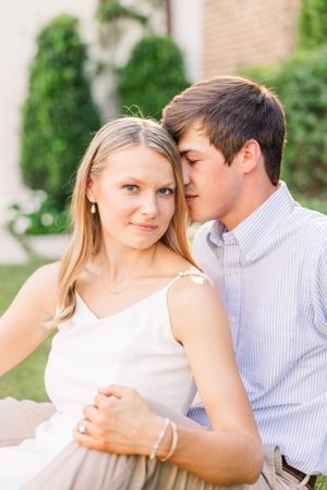 A romantic couple embraces outdoors with greenery in the background for their engagement photos.