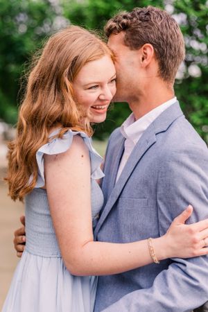 A tender moment between a couple in coordinating blue and grey outfits against greenery.