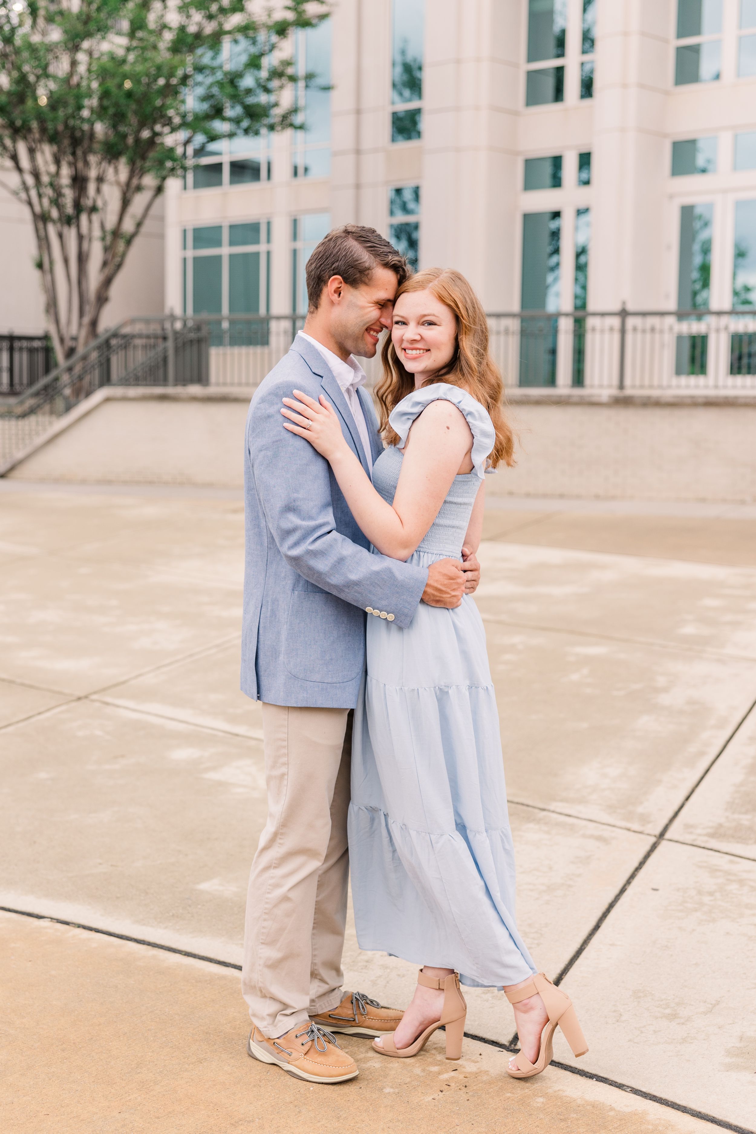 Couple in light blue and khaki sharing tender moment outside modern building.