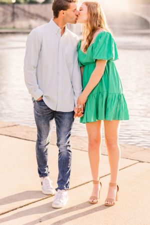 A couple sharing a kiss by the water, wearing casual attire on a sunny day.