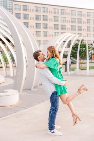 Couple embraces under modern curved white architecture with woman in green dress lifted off the ground.