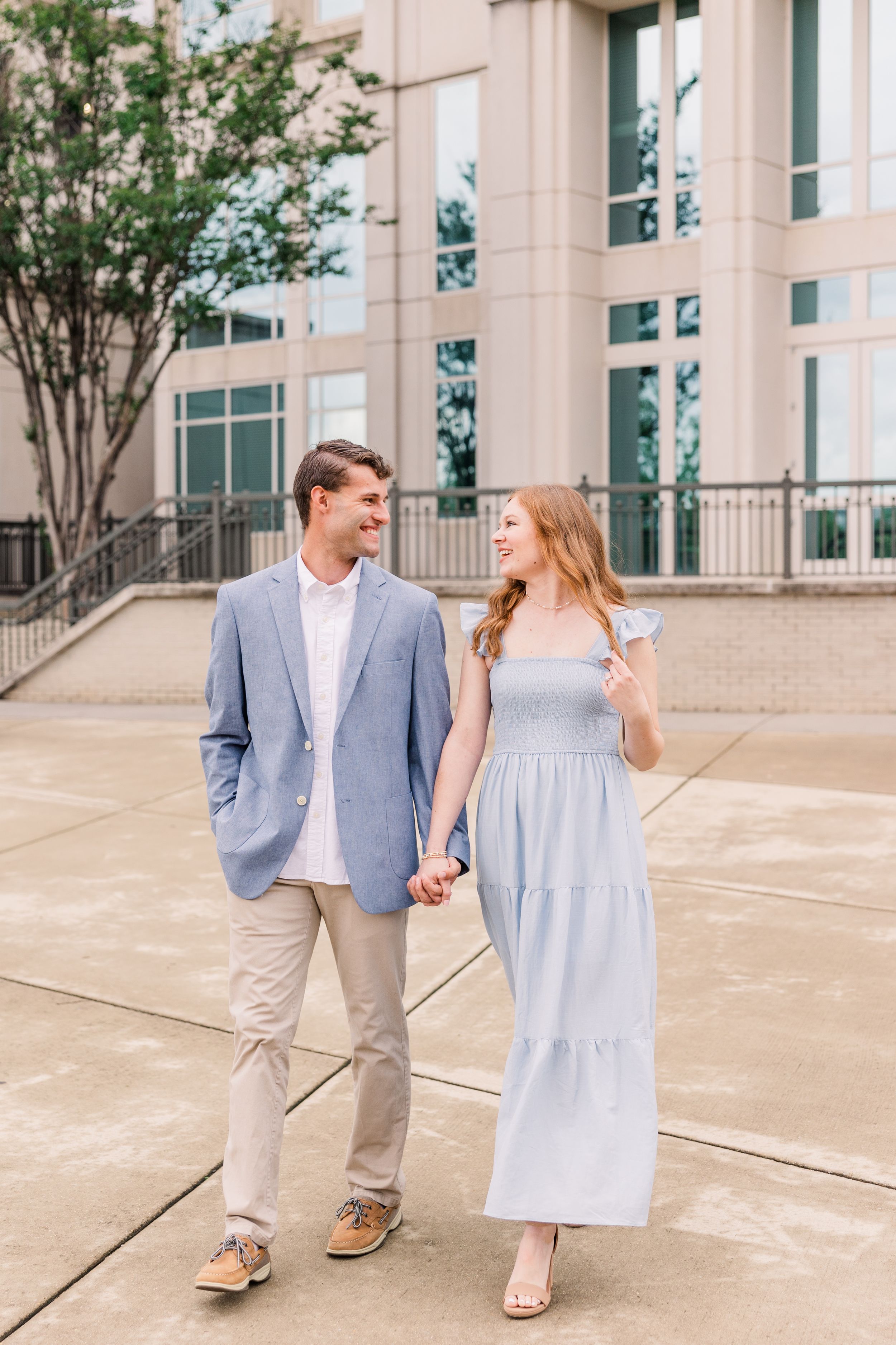 A couple walking and holding hands on a paved walkway, with the woman wearing a light blue maxi dress.