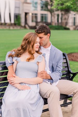 Intimate portrait of a couple sitting close together on a bench with a manicured lawn in background.