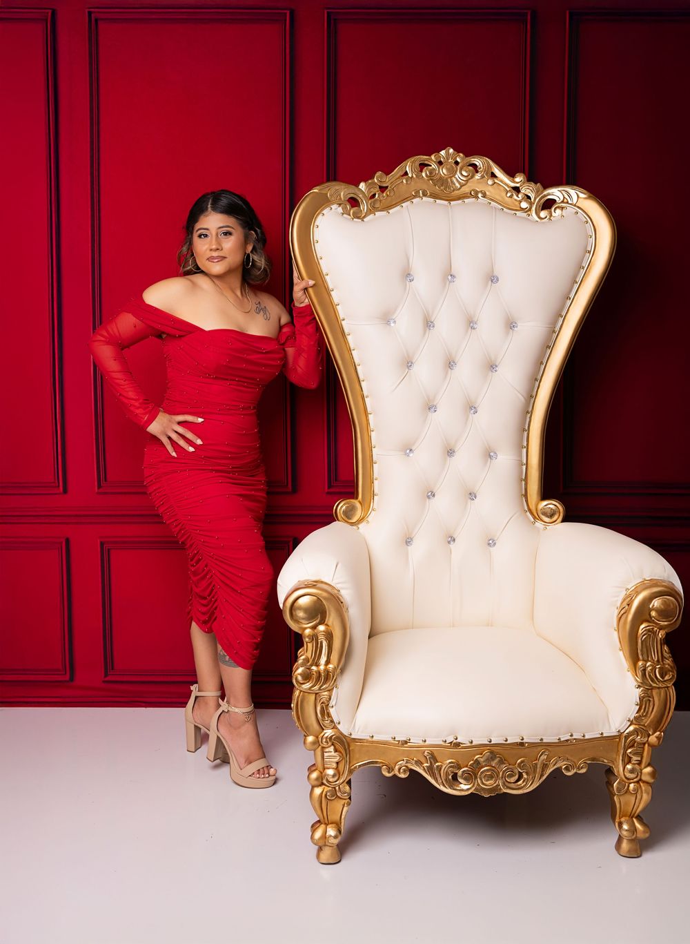Elegant baroque-style white and gold throne chair against deep red walls creates a luxurious studio photography setting.