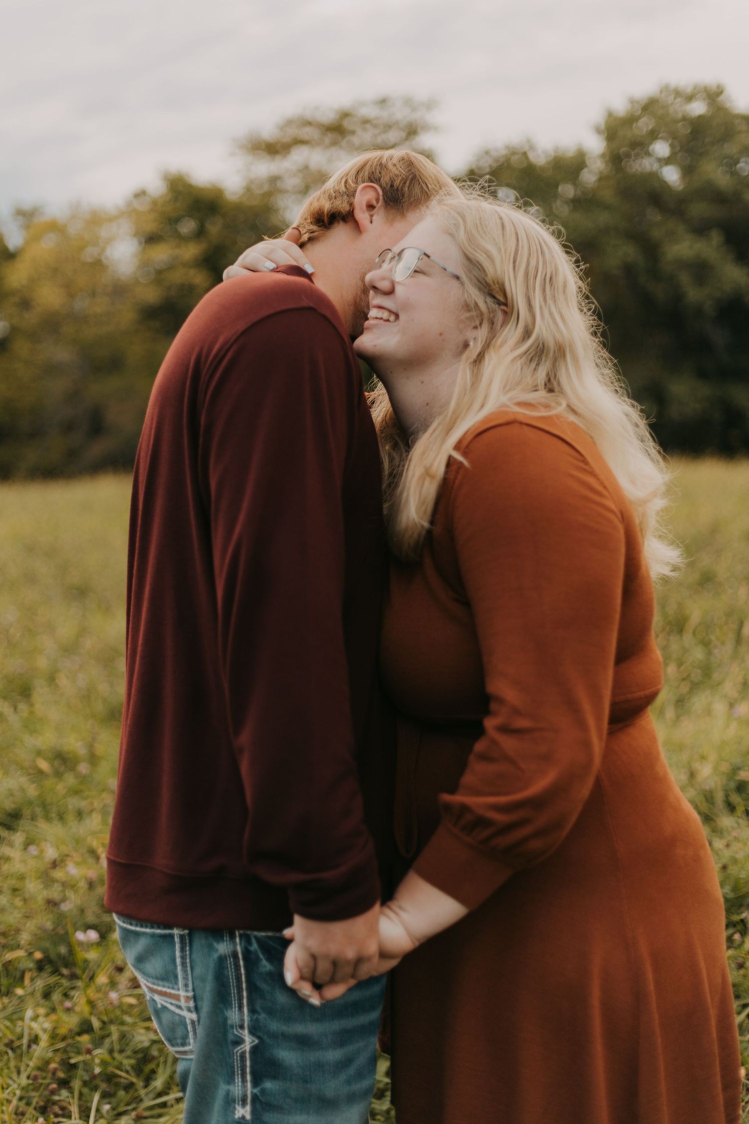 A couple in rust-colored sweaters share an intimate moment in a sunlit field.