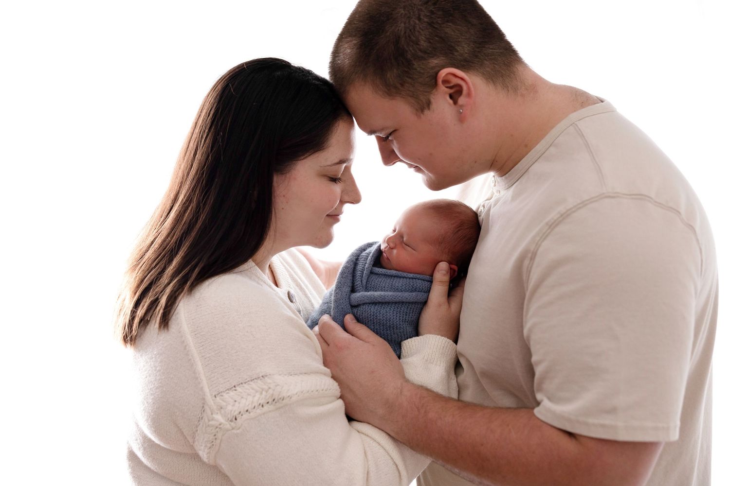 New parents tenderly holding their swaddled newborn baby together against a white background.