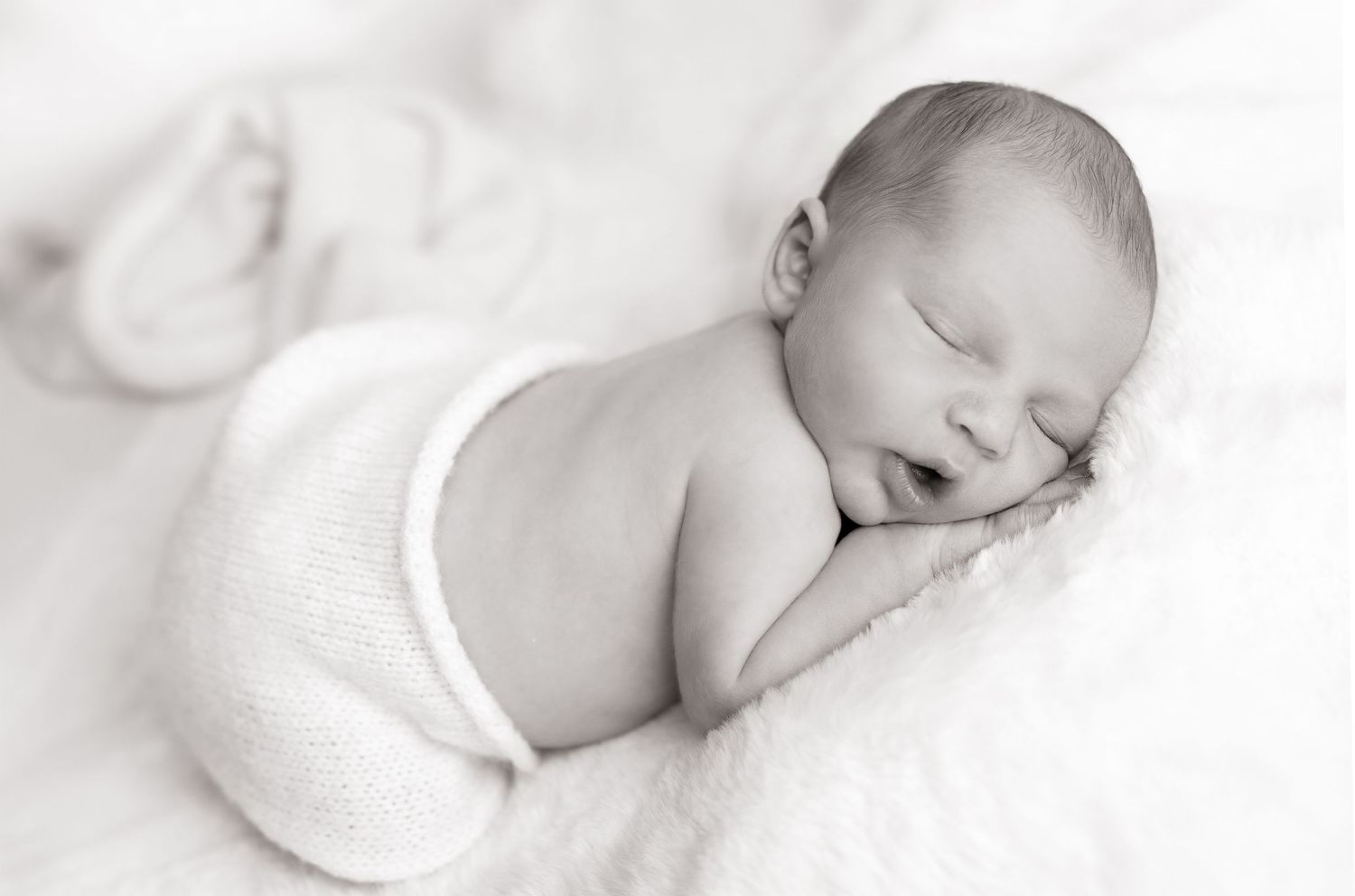 Peaceful newborn baby sleeping curled up on soft white blanket in black and white photography.
