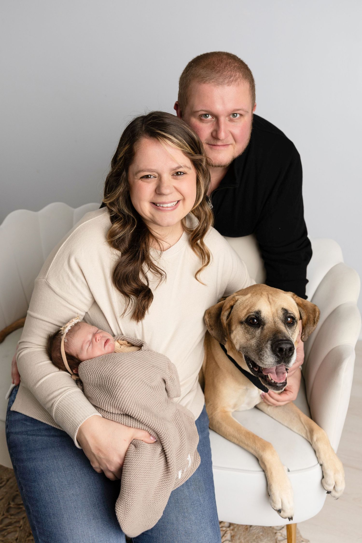 Family portrait on white chair with large dog showing warm expressions and casual attire.