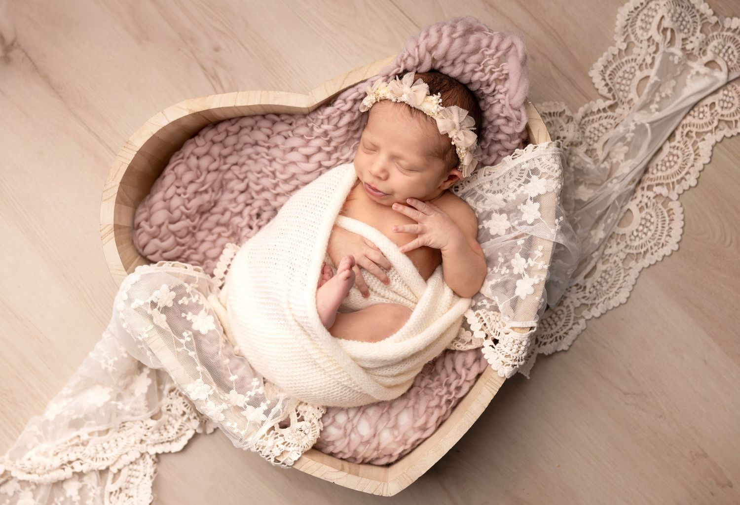Newborn sleeping in vintage basket with lace details and knit blanket.