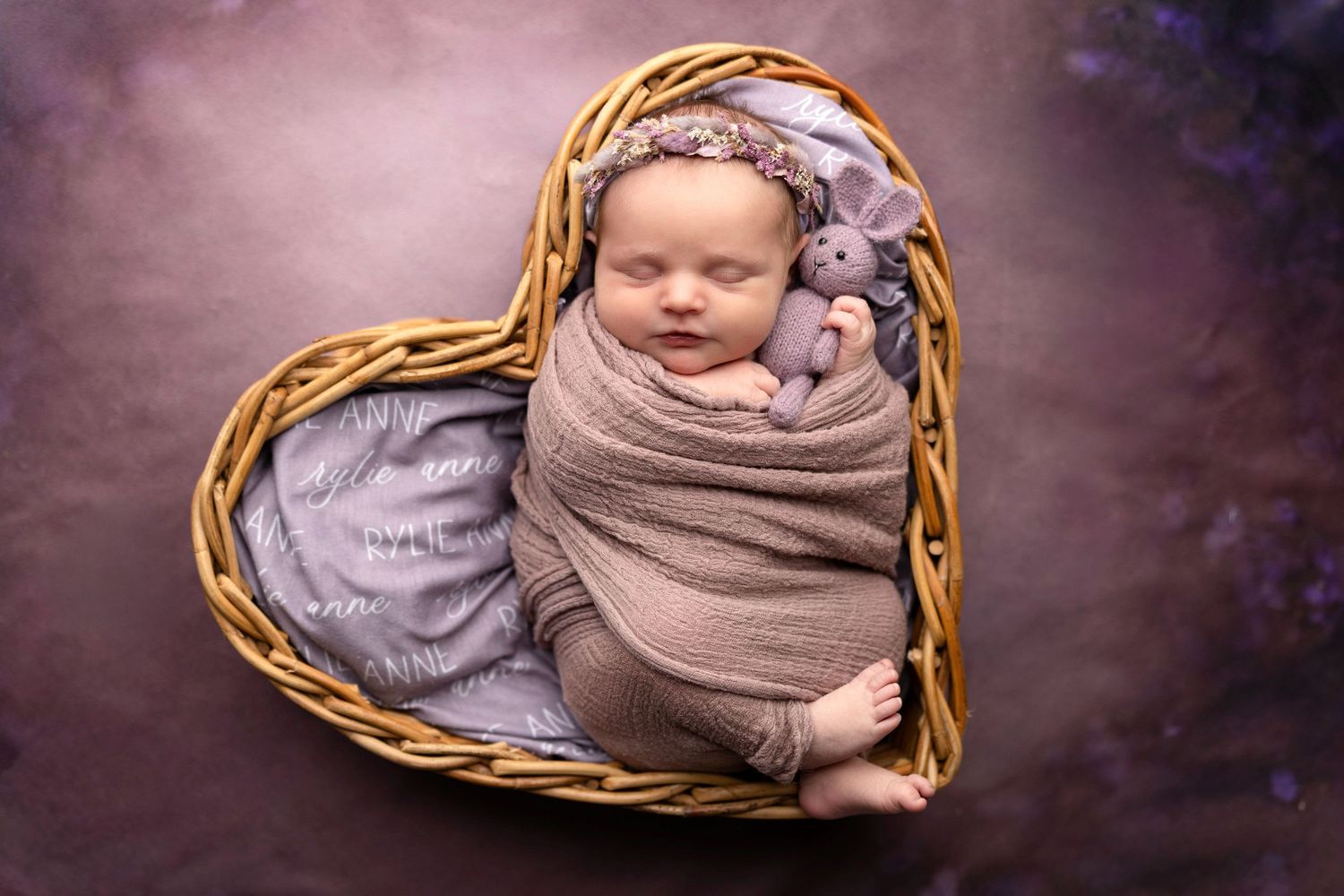 Artistic newborn photography in woven basket with purple backdrop.