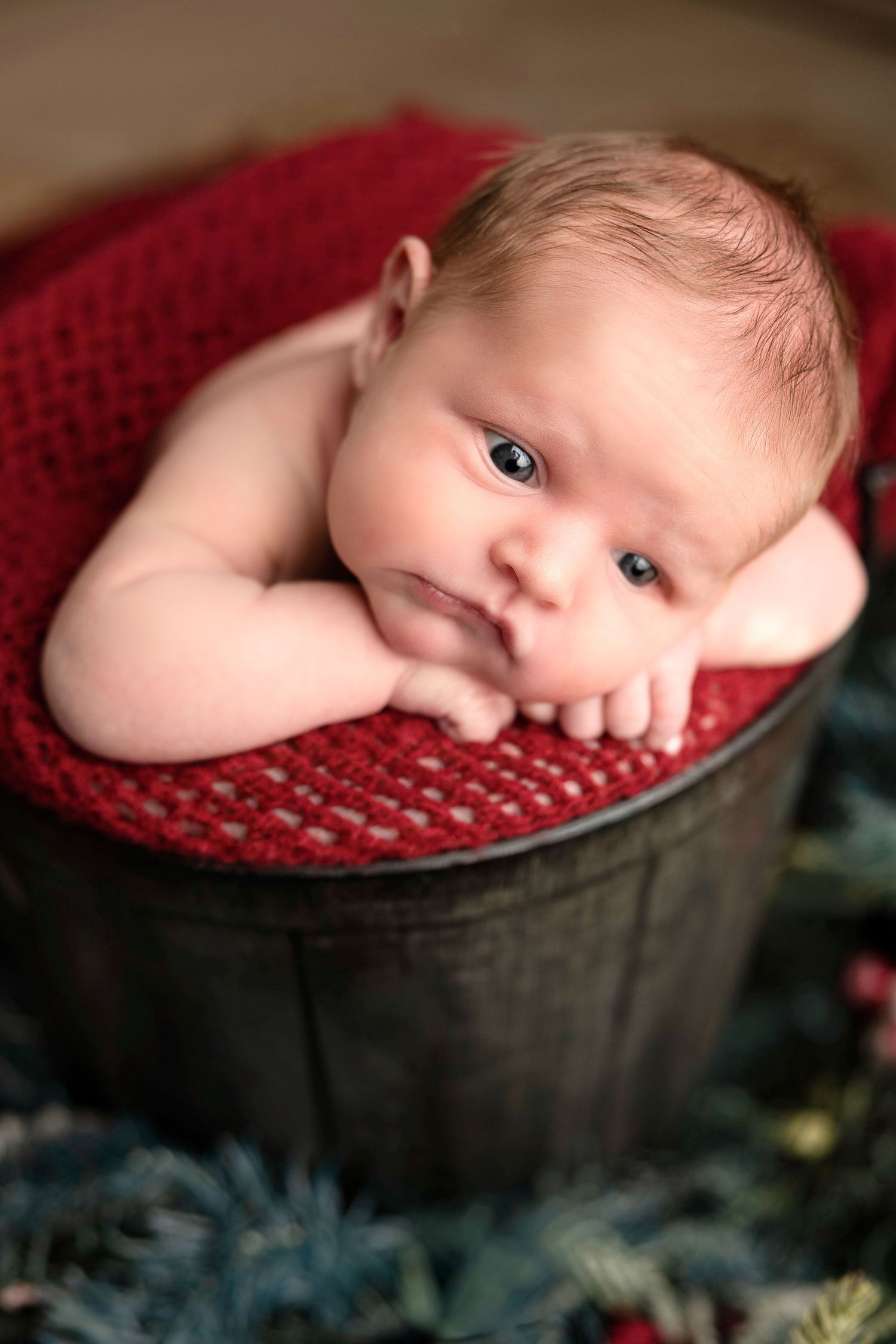 Close-up newborn portrait on red knit blanket with vintage styling.