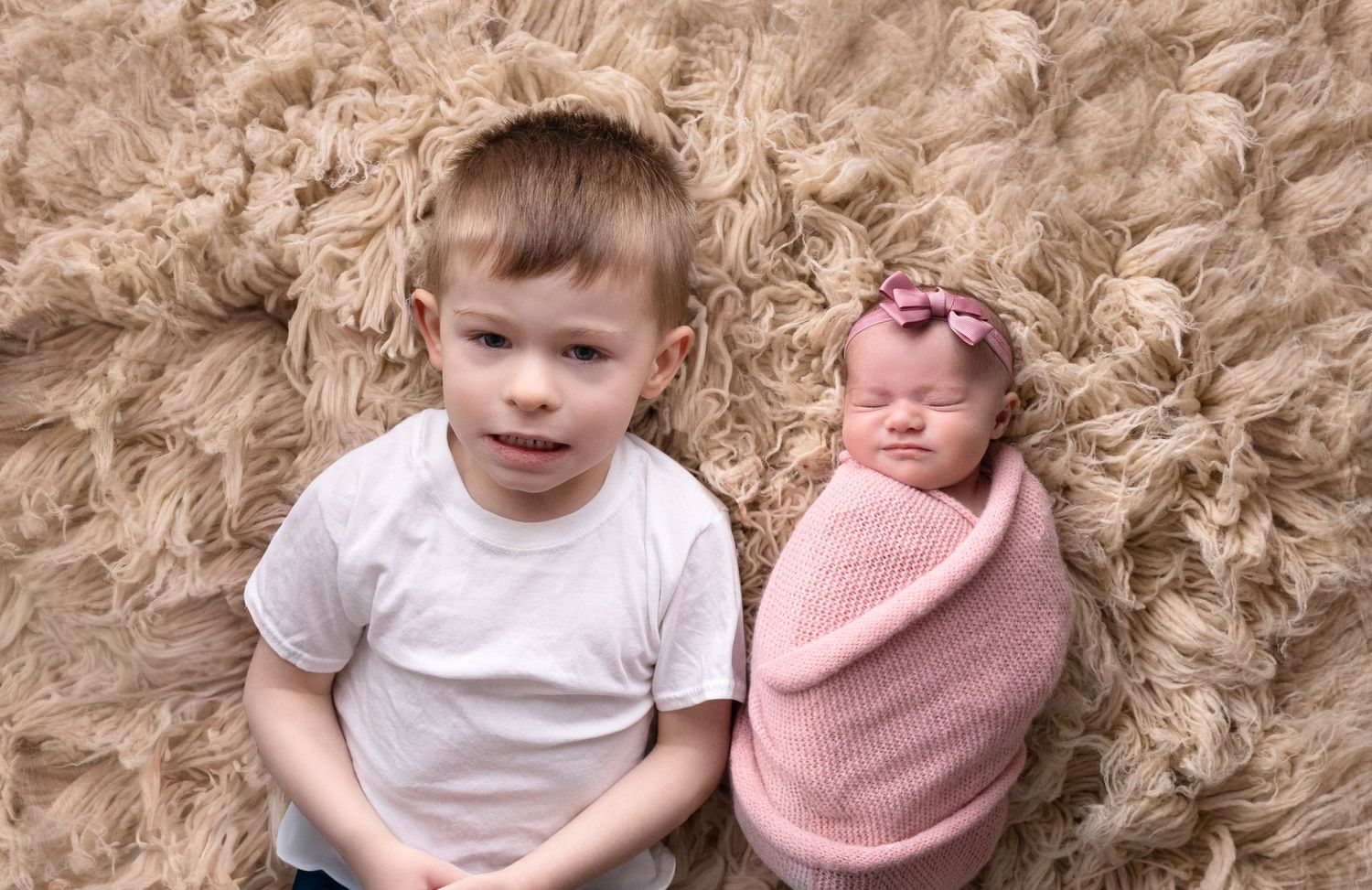 Siblings portrait on fluffy beige carpet showing tender moment.